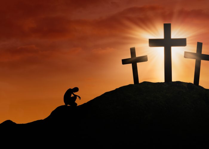 Silhouette of a man is praying for hope by the Cross under sunset background